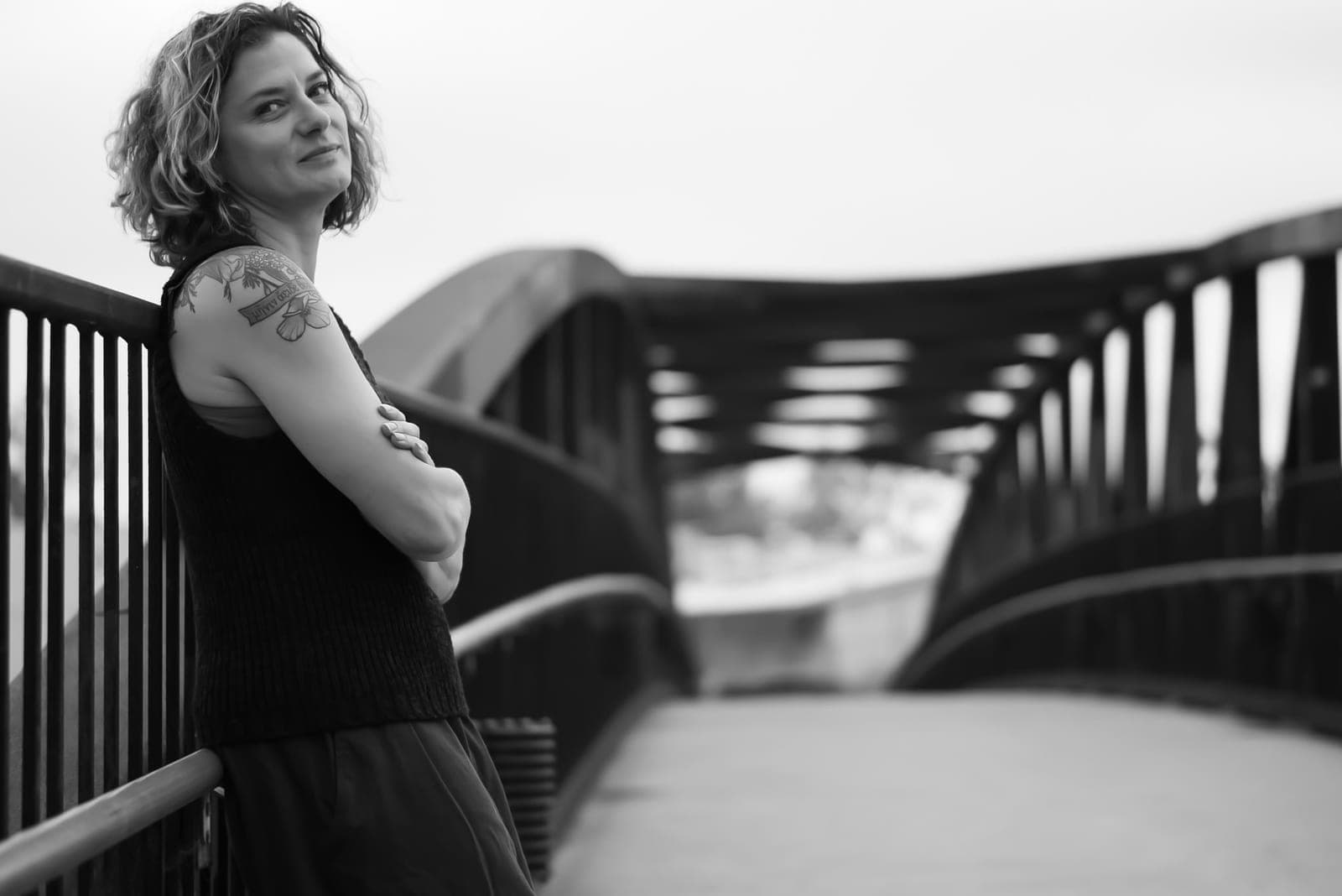 Ivy Pochoda leaning on the railing of a steel footbridge, arms folded, looking back over her shoulder